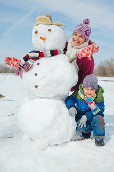 Happy beautiful children with snowman outside in winter time