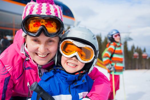 Portrait closeup of happy smiling boy in ski goggles and a helmet with his mother