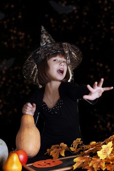 Witch child with pumpkin making magic on halloween, black background