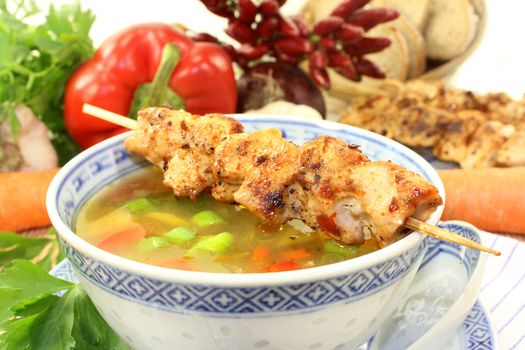 a bowl of chicken consomme and a chicken skewer