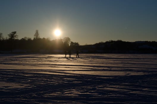 Three people silhouette walk on frozen lake snow and beautiful sunset light in evening.