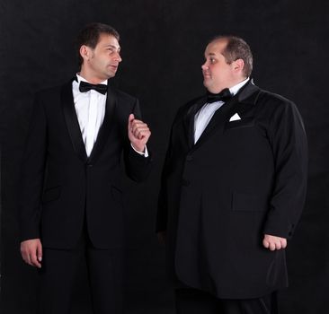 Two stylish businessman in tuxedos, on black background