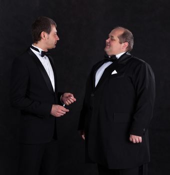 Two stylish businessman in tuxedos, on black background
