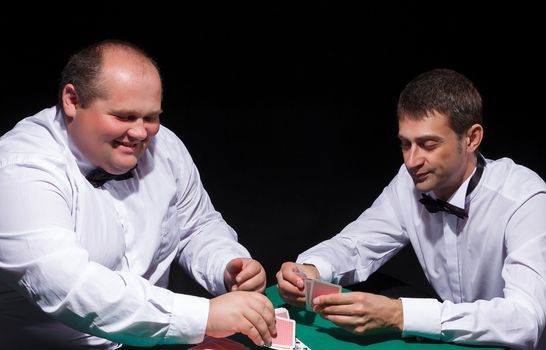 Two gentlemen in white shirts, playing cards, on black background