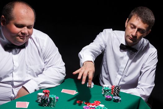 Two gentlemen in white shirts, playing cards, on black background
