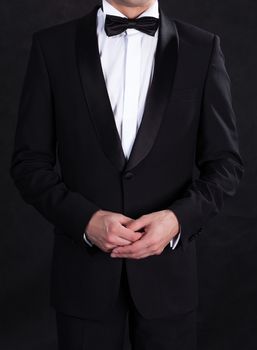 Stylish man in elegant black tuxedo, on black background