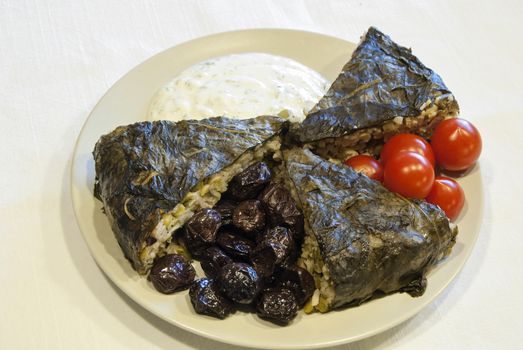 Homemade pie with rice, olives, vegetables, covered with vine leaves, garnished with cherry tomatoes and yogurt with chopped cucumber and garlic