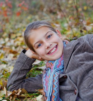 Portrait of happy girl lying on autumnal ground covered with dry leaves