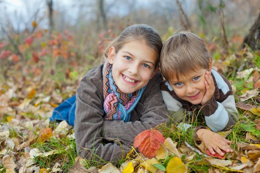 Happy kids lying on autumnal ground covered with dry leaves