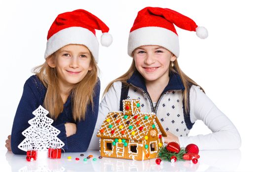 Christmas theme - Two smiling girl in Santa's hat with gingerbread house, isolated on white