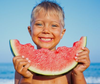 Handsome boy eating slice of watermelon on the beach