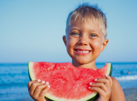Handsome boy eating slice of watermelon on the beach