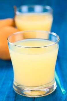 Pear juice in glass with drinking straws on the side and Bosc pear in the back on blue wood (Selective Focus, Focus on the front rim of the glass)