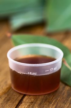 Eucalyptus cough syrup in medicine cup with fresh Eucalyptus leaves (Selective Focus, Focus on the 15ml sign on the cup)