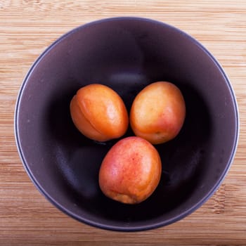 Three apricots inside a brown cup over wooden background