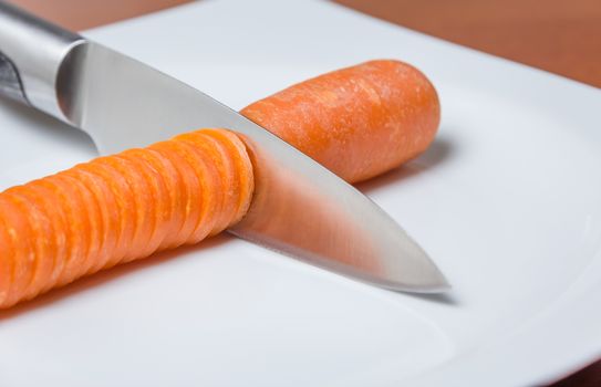 Knife slicing carrot in a white plate over wooden table