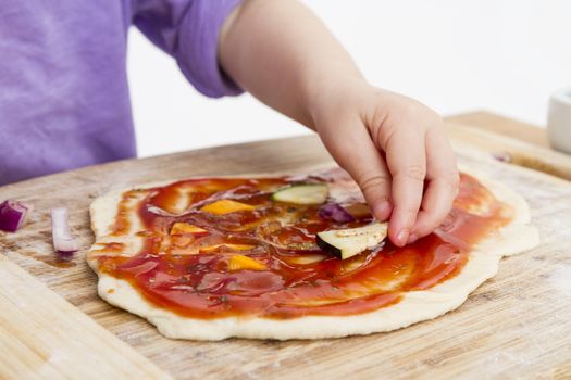 hand of young child making pizza on wooden board