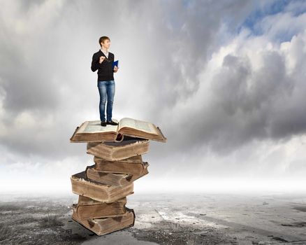 Image of little cute boy standing on pile of books