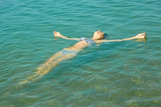 Teen girl lying on the turquoise sea water surface in shallow coastal area