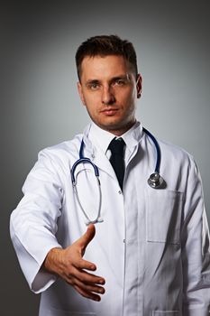 Medical doctor with stethoscope giving hand for handshaking against grey background 