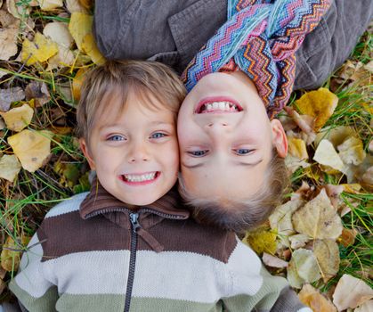 Happy kids lying on autumnal ground covered with dry leaves