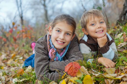 Happy kids lying on autumnal ground covered with dry leaves