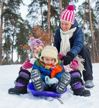 Two kids with mother is sledging in winter-landscape