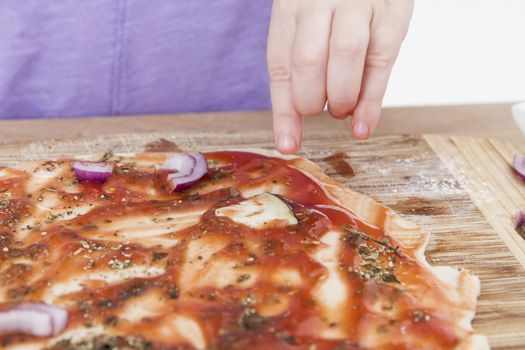 hand of young child making pizzaon wooden board