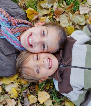 Happy kids lying on autumnal ground covered with dry leaves