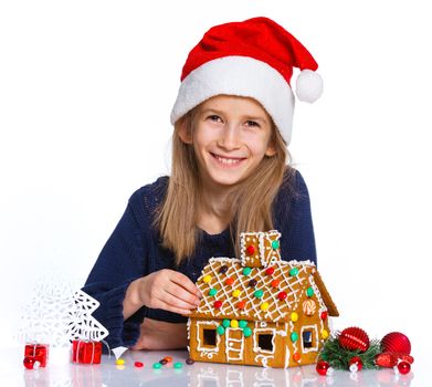 Christmas theme - Smiling girl in Santa's hat with gingerbread house, isolated on white