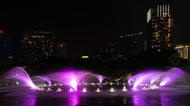 Illuminated lilac fountain at night in dark city skyline 