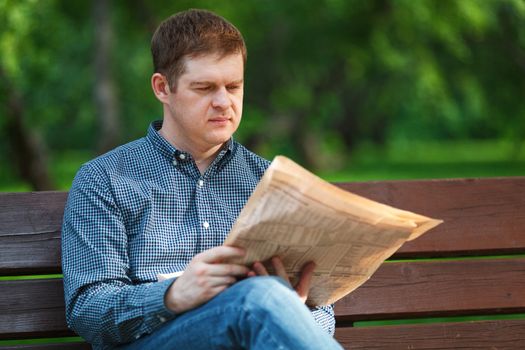Man reads a newspaper on a bench in the park