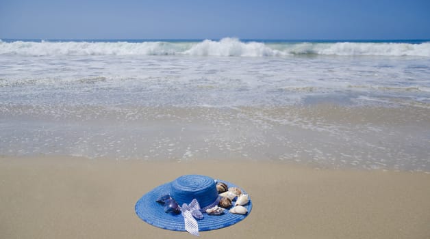 Blue woman's summer hat with seashells on a sand by the ocean
