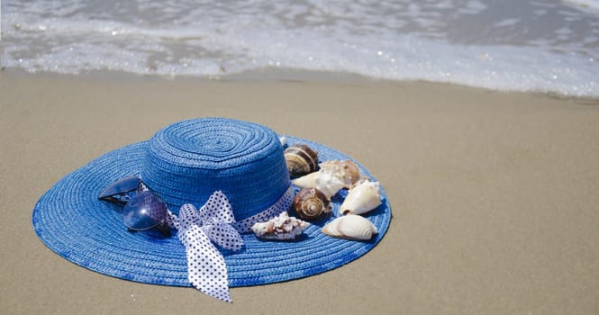 Blue summer woman's hat with seashells on beach's sand