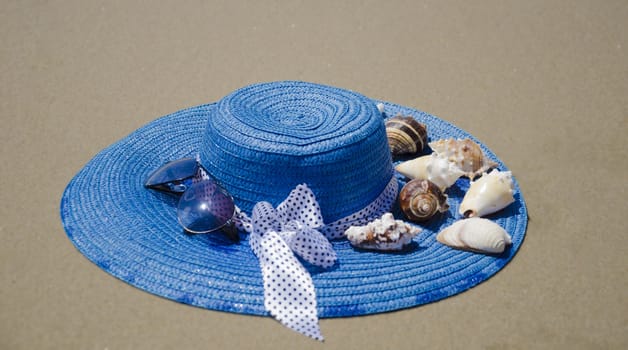 Blue summer woman's hat with seashells on beach's sand 