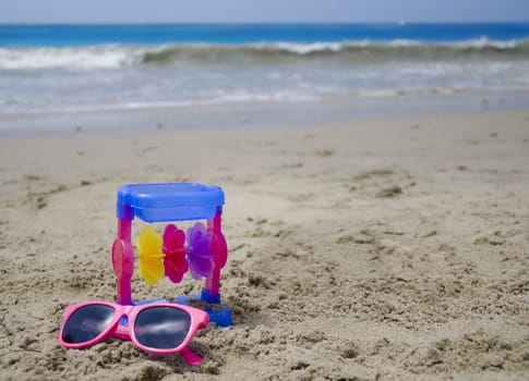 Colorful child's toy and sunglasses on a beach's sand by the ocean
