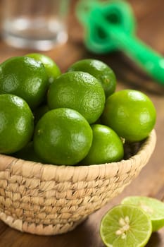 Limes in woven basket with lime squeezer and glass in the back (Selective Focus, Focus on the two upper limes) 