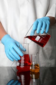 Latex gloved hands pouring liquads into a flask in a laboratory