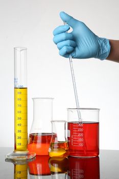 Laboratory Glassware with fluids and gloved hand hand a measuring pipette