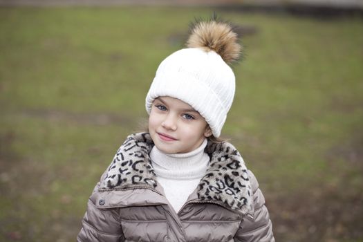 Portrait of beautiful little girl in a white knitted hat autumn