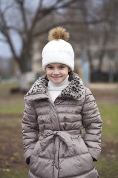 Portrait of beautiful little girl in a white knitted hat autumn