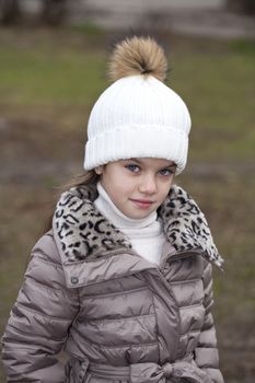 Portrait of beautiful little girl in a white knitted hat autumn