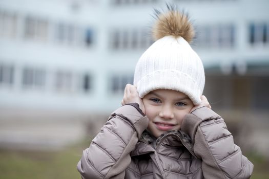 Portrait of beautiful little girl in a white knitted hat autumn