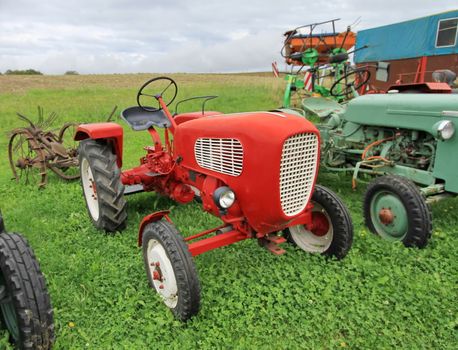 Close up of red antique tractor on green grass by cloudy day