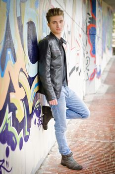 Attractive blond haired young man standing against graffiti wall