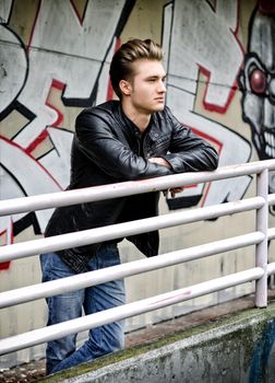 Handsome blond haired young man leaning on metal railing, in urban environment