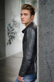 Attractive blond young man in city environment, standing against marble column