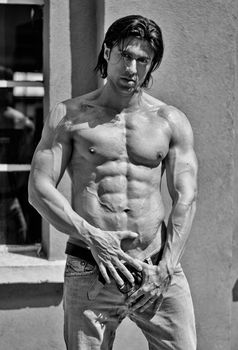 Muscular young bodybuilder shirtless outdoors in jeans, black and white shot
