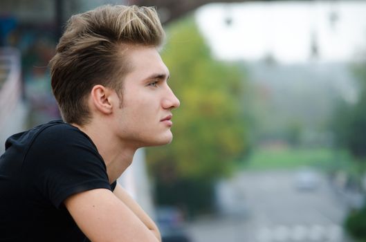 Profile  shot of attractive blond young man in city, looking afar outdoors