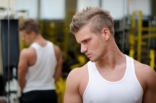Handsome young man in gym resting and looking down to a side, wearing tanktop